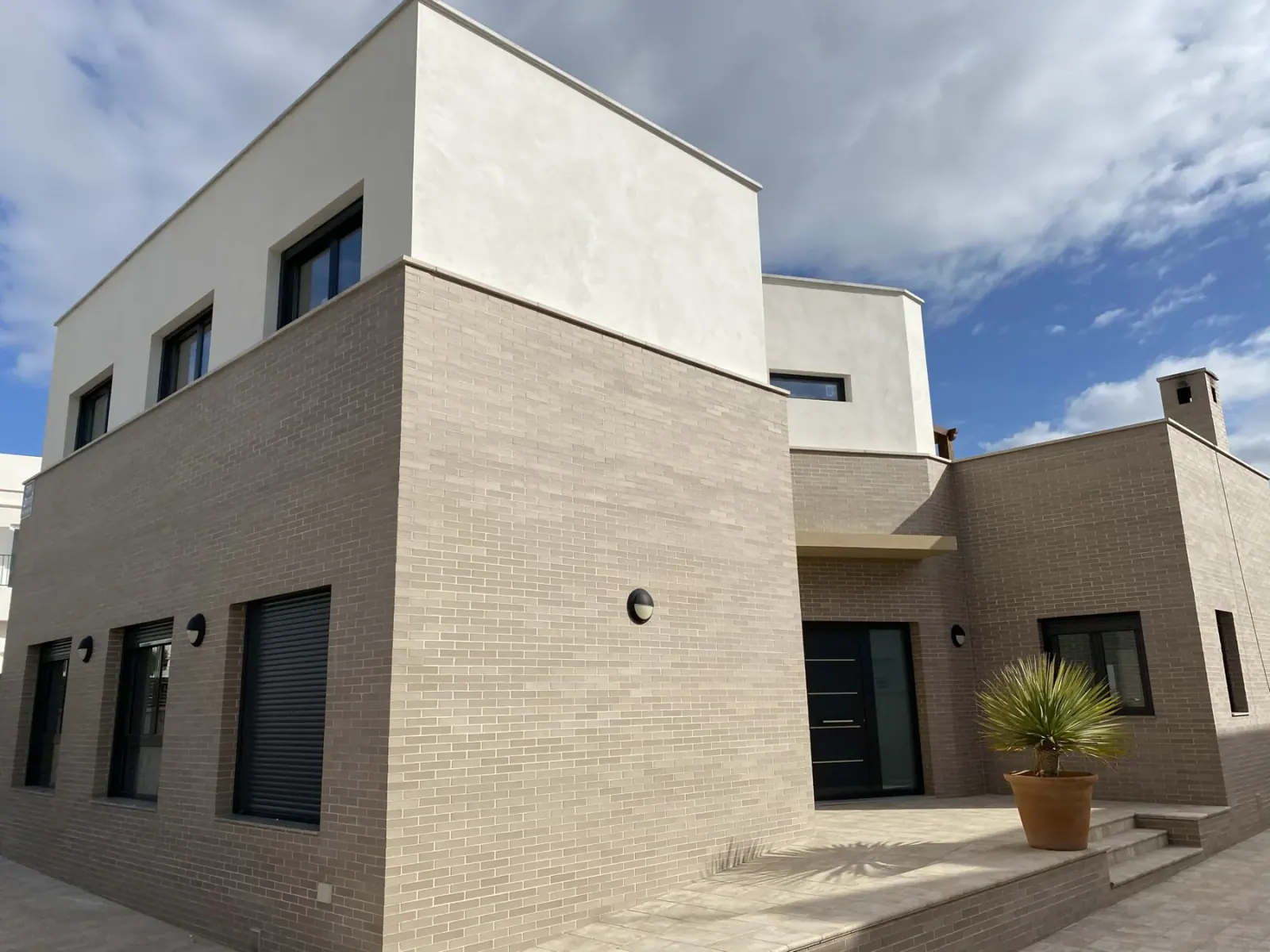 Fachada de vivienda con piedra, volúmenes blancos y jardín
